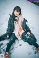 A woman sitting in the snow wearing a black jacket and orange bikini.